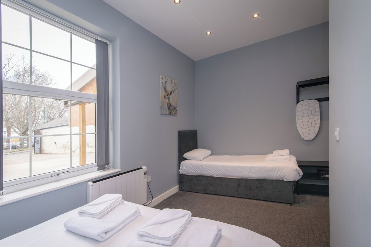 A modern bedroom with a large window, a bed, a bedside table with towels, and a radiator.