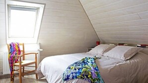 Ett sovrum med ett sluttande tak, en säng med vita sängkläder, en färgglad pläd och en stol med en färgglad filt.