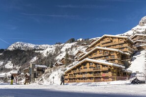 A multi-story wooden chalet with balconies, set against a snowy mountain backdrop. - Wifi, 20m from ski slopes, fitness, swimming pool, sauna, hammam, terrace, balcony, tv, ski locker (Le Grand-Bornand)