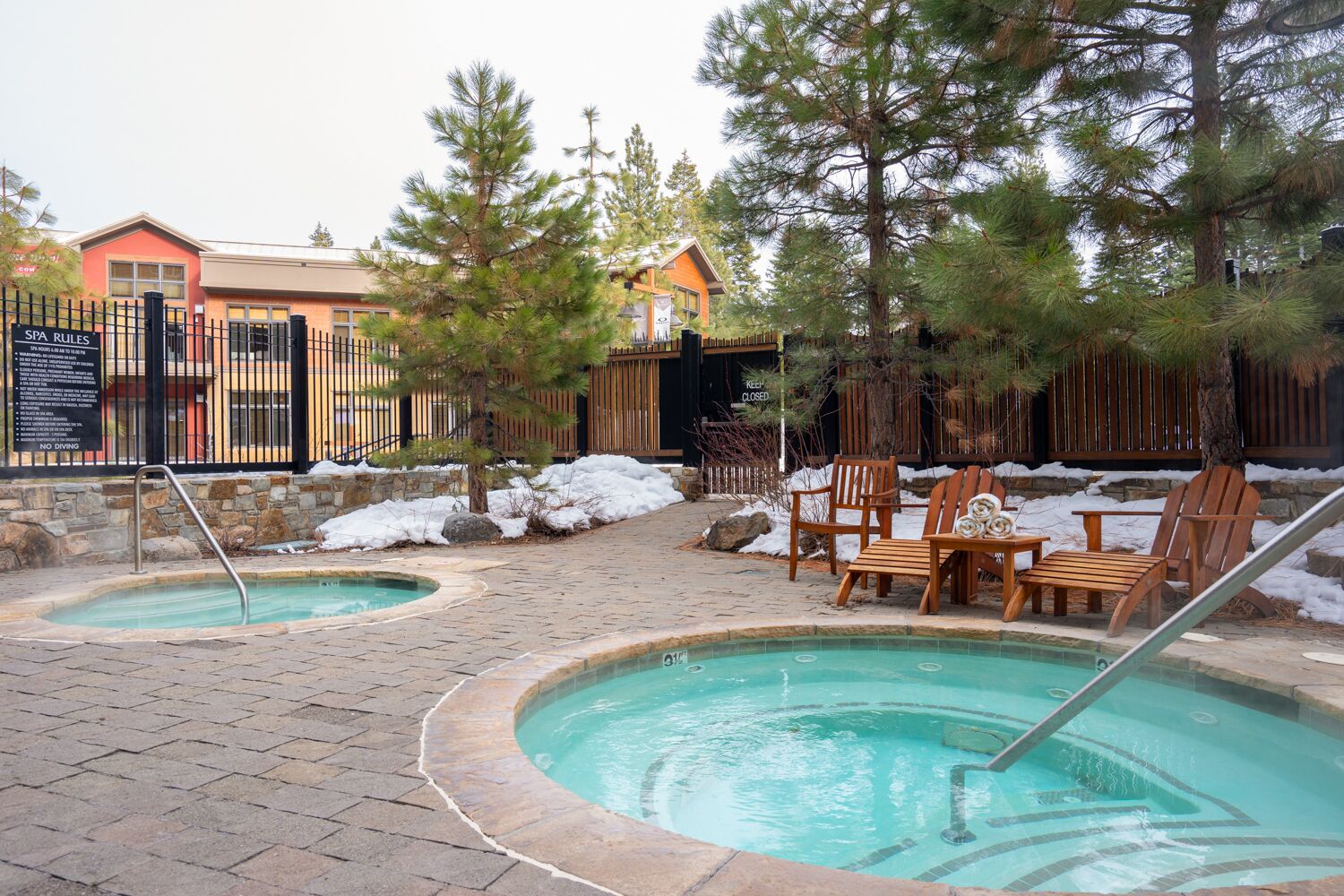 A pool area with two hot tubs, wooden chairs, and a stone pathway.