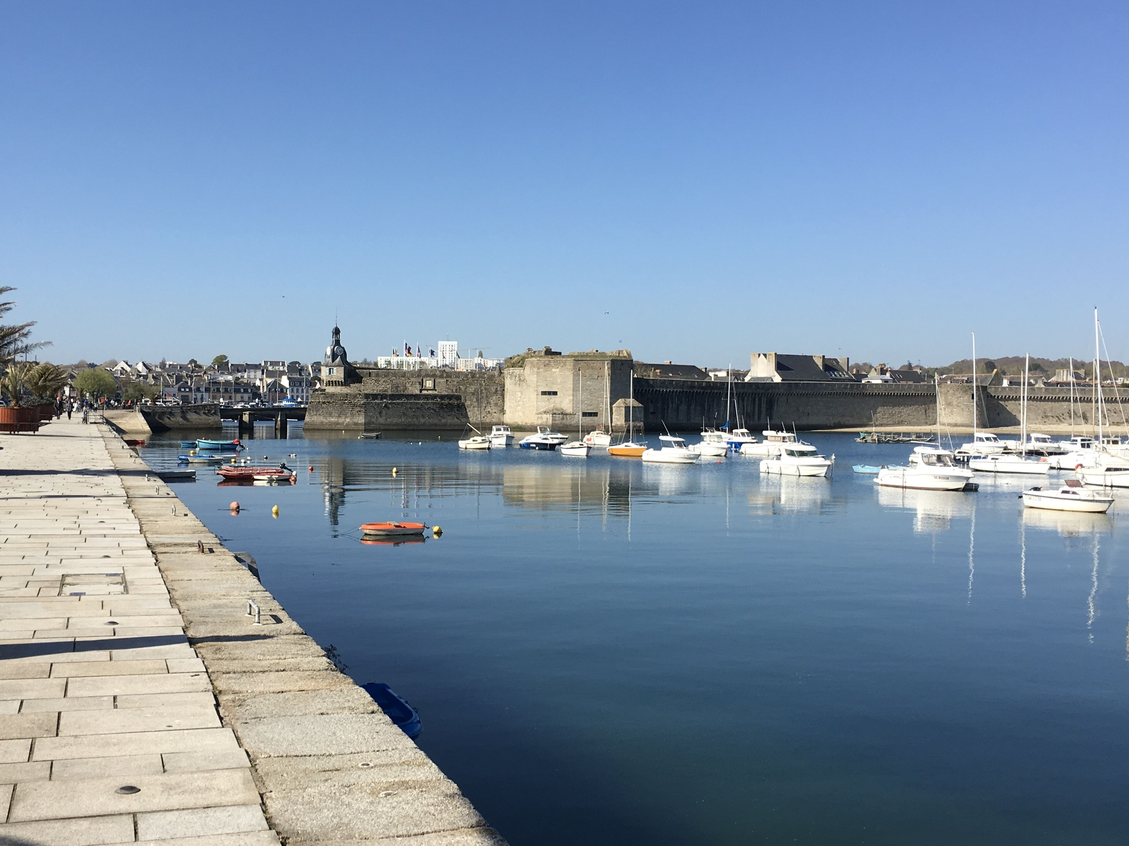 Un port où des bateaux sont amarrés, un mur de pierre et un ciel dégagé.