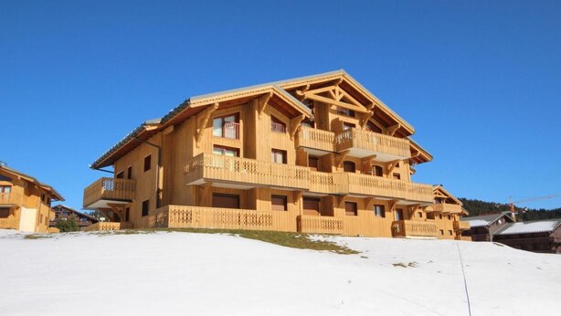A multi-story wooden chalet with balconies, set against a snowy landscape.