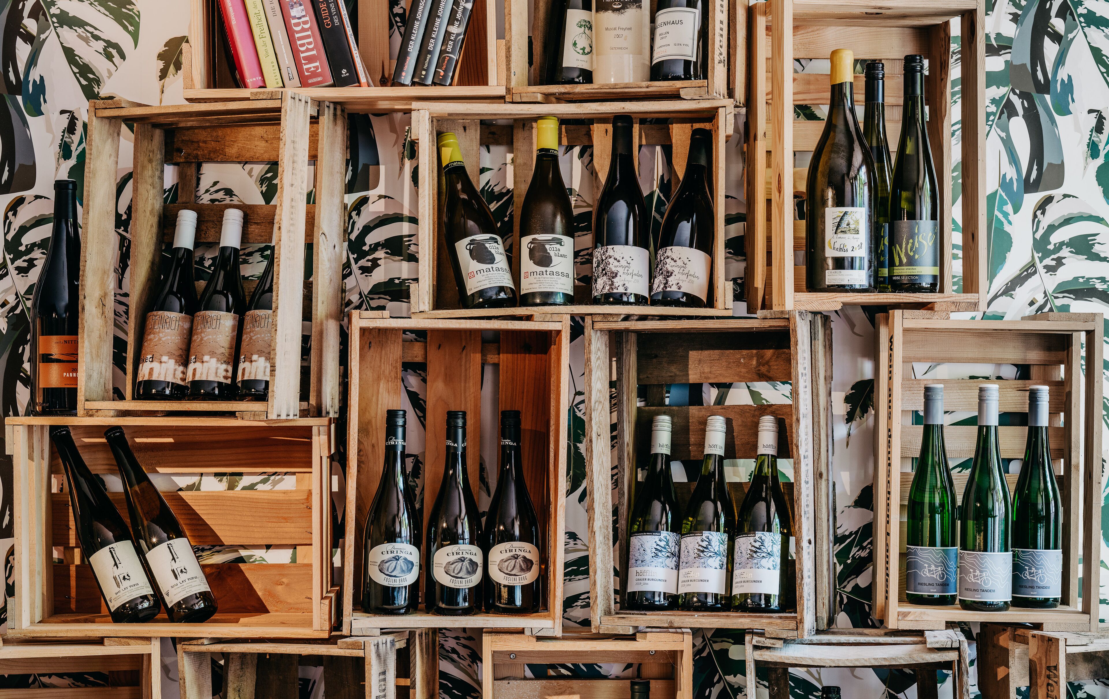 Una colección de cajas de madera llenas de botellas de vino, dispuestas frente a un fondo de papel tapiz estampado.
