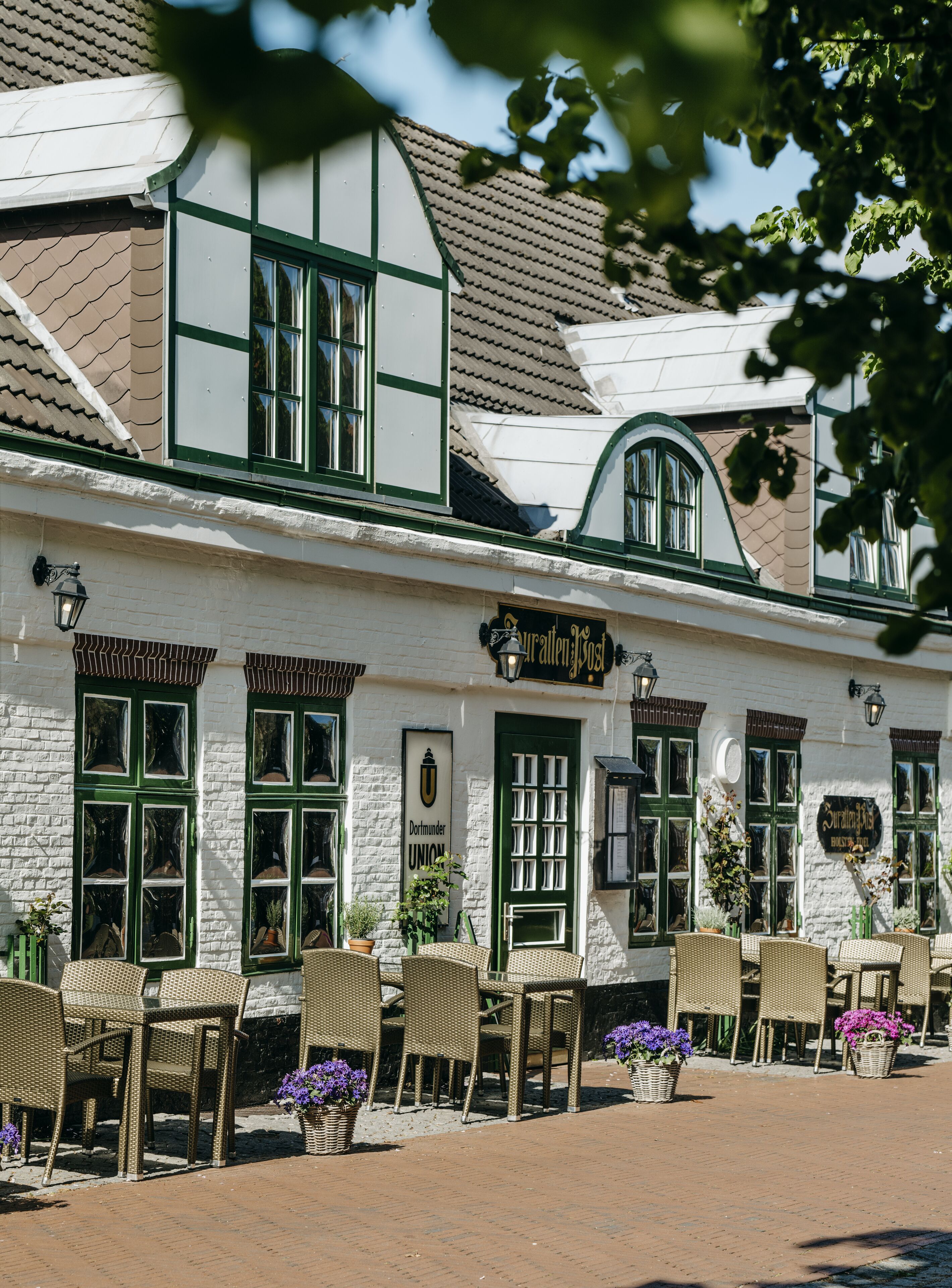 A traditional building with a white facade and green accents, featuring outdoor seating and potted plants.