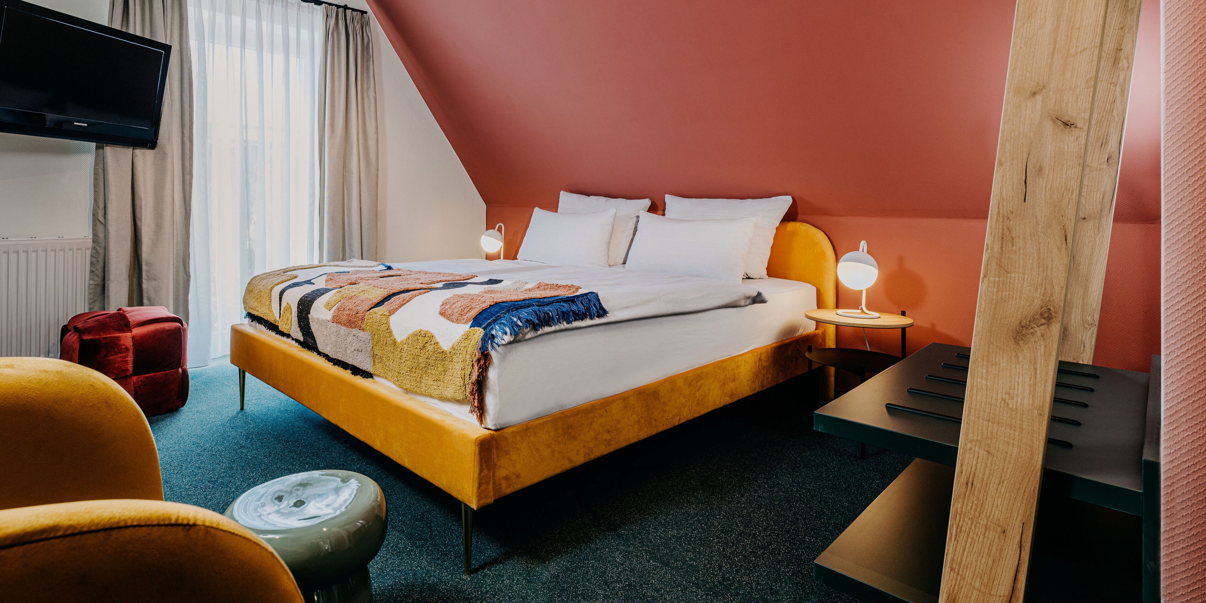 Een hotelkamer met een bed, nachtkastje, lamp, televisie en rode koffer.