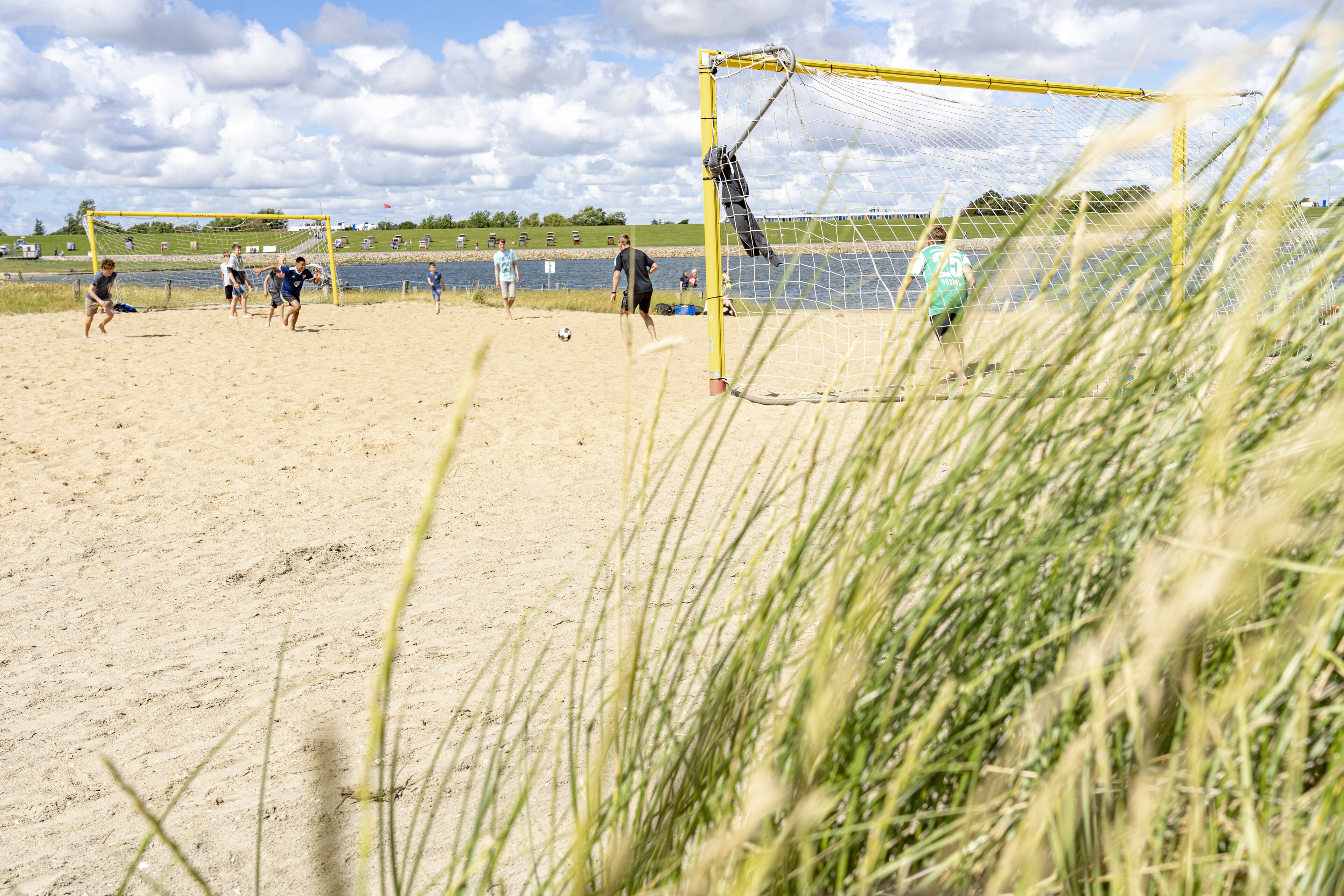 A beach soccer game with a goalpost and players.