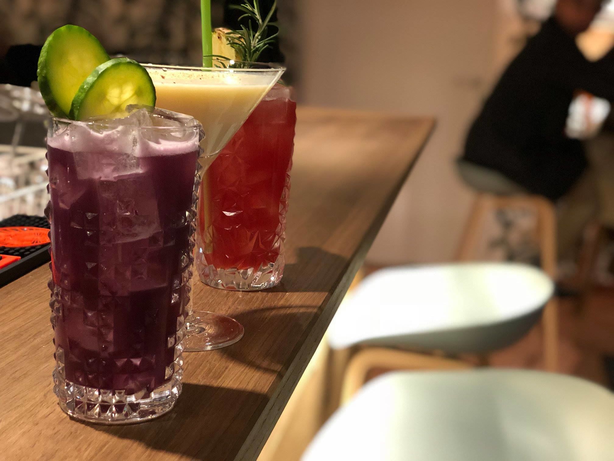 Two glasses of beverages on a wooden bar counter.