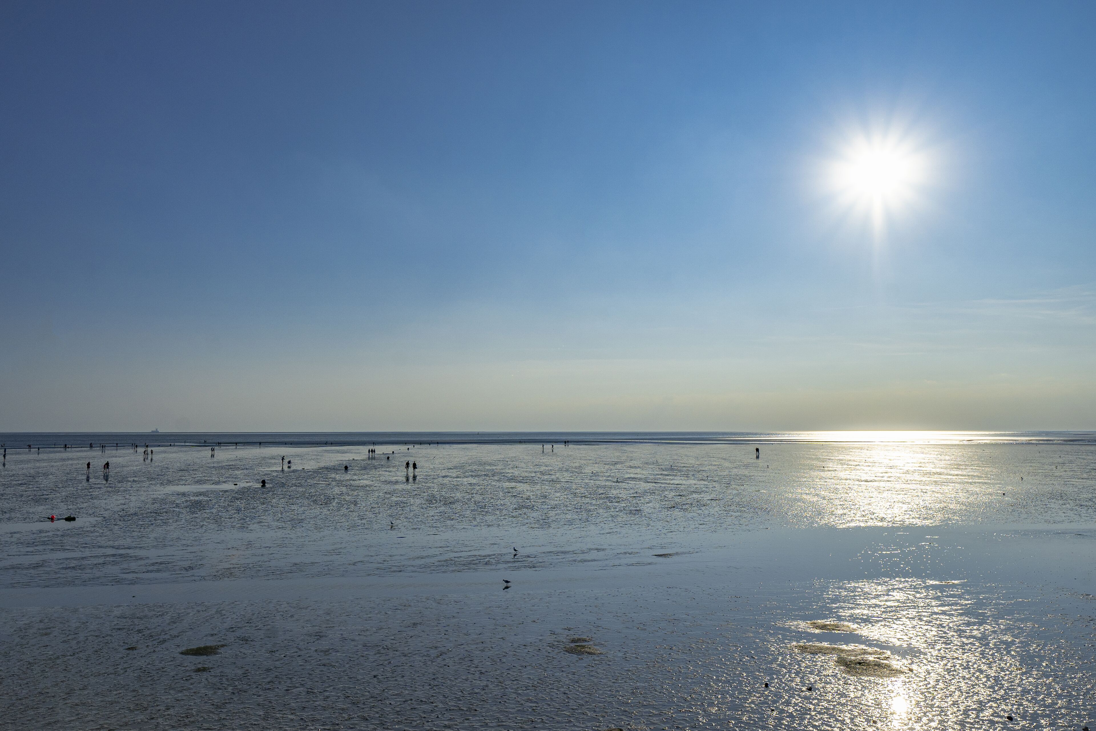 A beach with people walking and sun reflecting on the water.