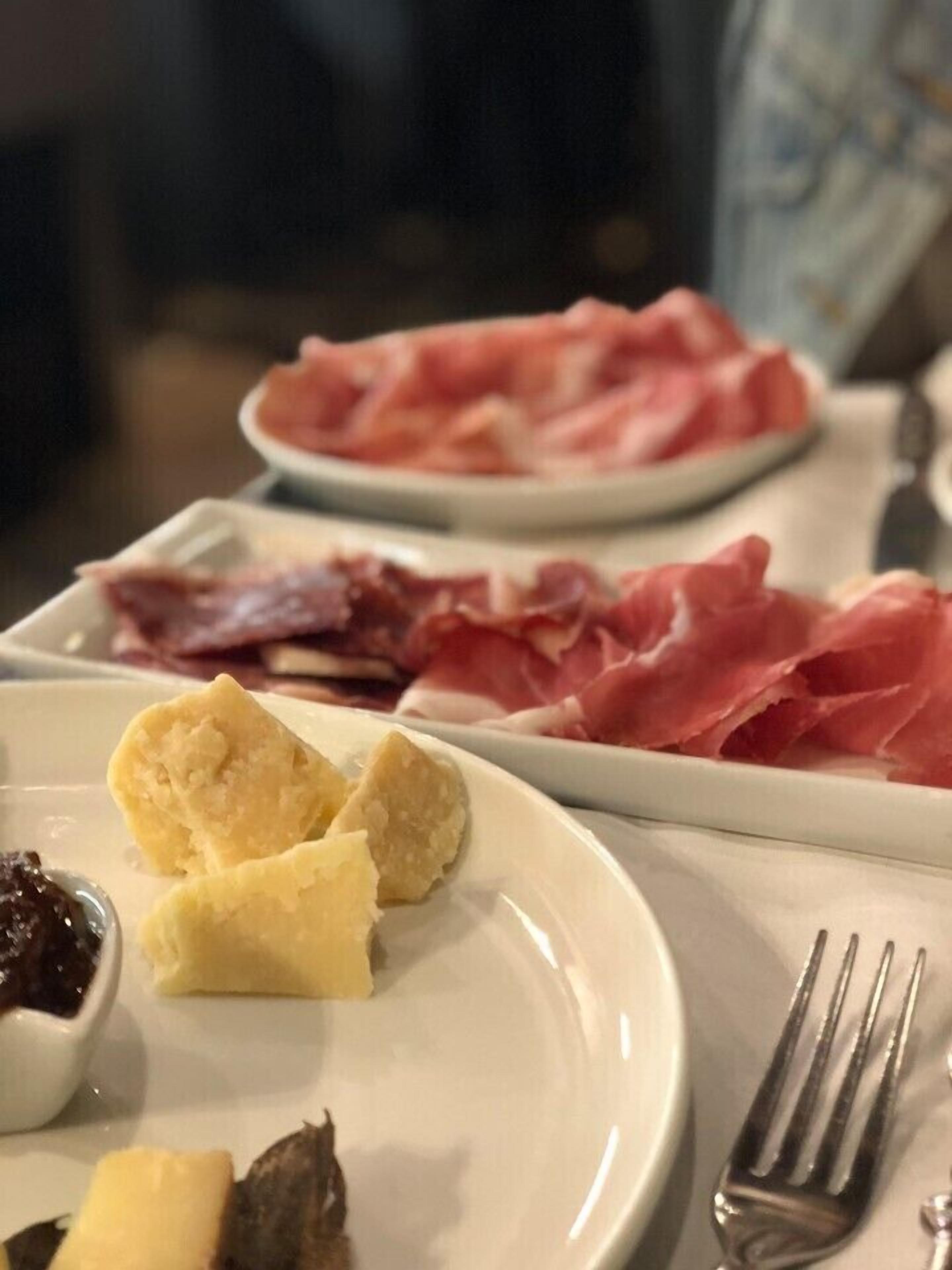 A plate with various food items including cured meats, cheese, and a small bowl of jam.
