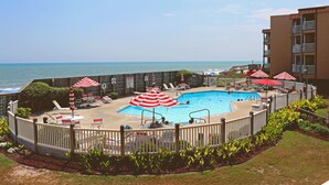 Ein Poolbereich mit Meerblick, umgeben von einer Einfriedung, mit Liegestühlen und Sonnenschirmen.