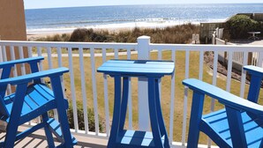 Ein Balkon mit blauen Stühlen und einem Tisch mit Blick auf einen Strand, Dünen und das Meer.