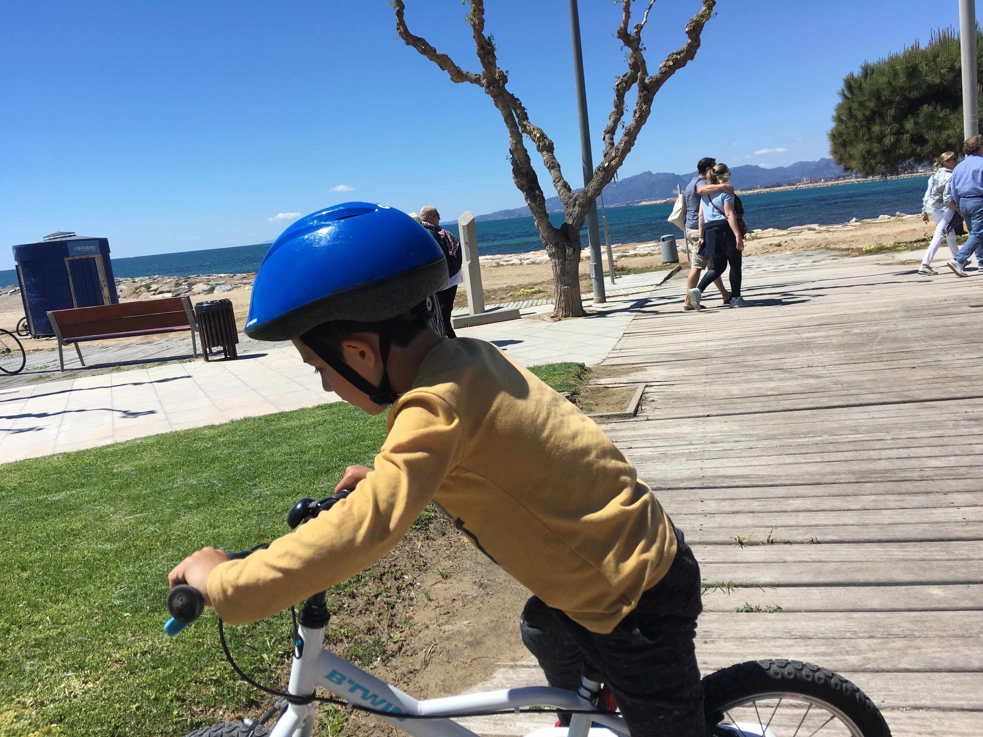 Niño montando una bicicleta en una pasarela de madera, con un banco y un bote de basura cerca.