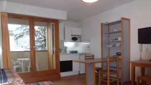 A cozy room with a sofa, a small table, a dining table with chairs, a kitchen area with a microwave, and a TV.