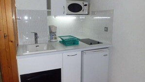 A compact kitchen with white cabinets, a microwave, a coffee maker, and a dishwasher.