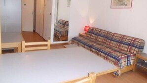A room with a bed, a sofa, a table, and a mirror.