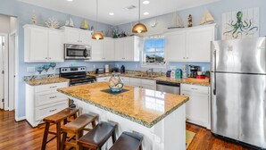 Una cocina moderna con armarios blancos, encimeras de granito, electrodomésticos de acero inoxidable y una isla central con taburetes de bar.