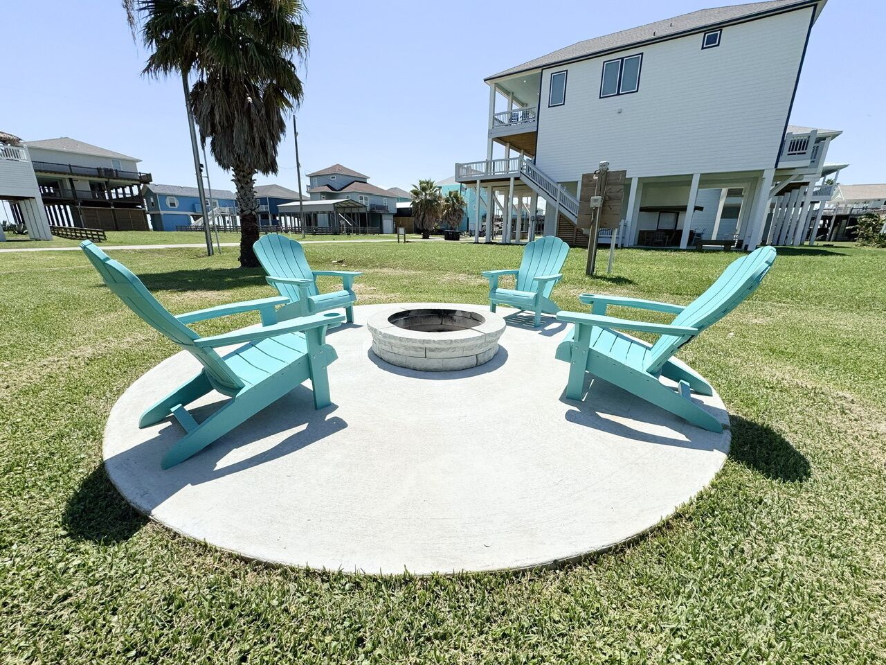 Een rond zitgedeelte buiten, met vier turquoise Adirondack-stoelen en een vuurkorf in het midden.
