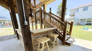 Un área de estar exterior con madera, piso de concreto y una escalera de madera, con vista a un edificio residencial al fondo.