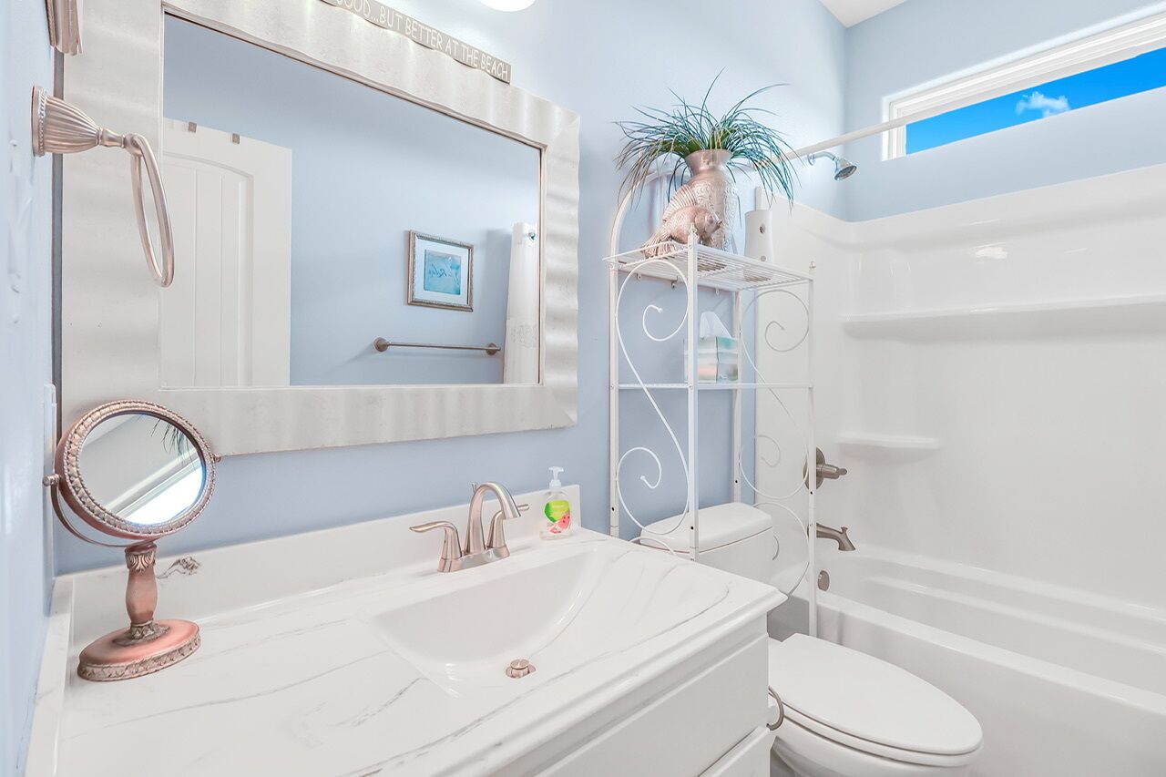 Une salle de bain avec un meuble-lavabo blanc, un grand miroir, un évier, des toilettes et une douche.