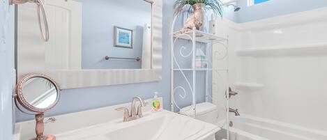 Une salle de bain avec un meuble-lavabo blanc, un grand miroir, un évier, des toilettes et une douche.