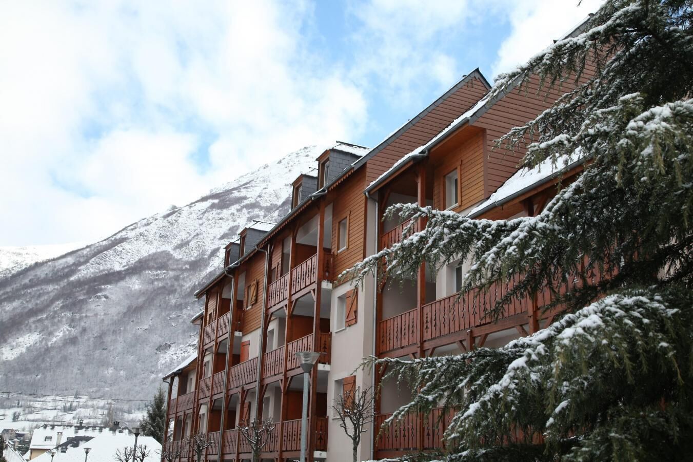 Un hôtel à plusieurs étages, doté de balcons, qui se dresse sur fond de montagnes enneigées.