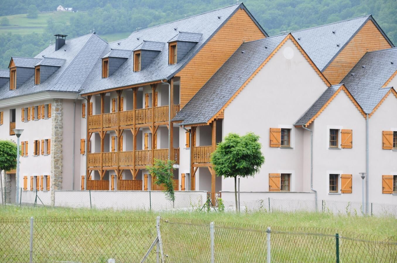 A row of multi-story buildings with a mix of stone and wood exteriors, featuring balconies and a fenced property.