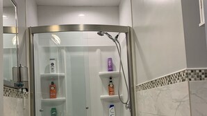 A bathroom with a glass-enclosed shower, a pedestal sink, and toiletries on shelves. - 2BR-Free Parking, Near Gillette & Providence-I-95 (Pawtucket)