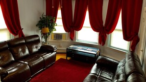 A living room with a brown leather sofa, a red rug, and a ceiling fan. - 2BR-Free Parking, Near Gillette & Providence-I-95 (Pawtucket)