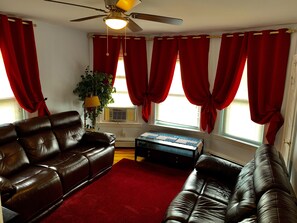 A living room with a brown leather sofa, a red rug, and a ceiling fan. - 2BR-Free Parking, Near Gillette & Providence-I-95 (Pawtucket)