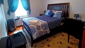 Un dormitorio con cama, ventilador de techo, mesita de noche, lámpara y ventana con cortinas.