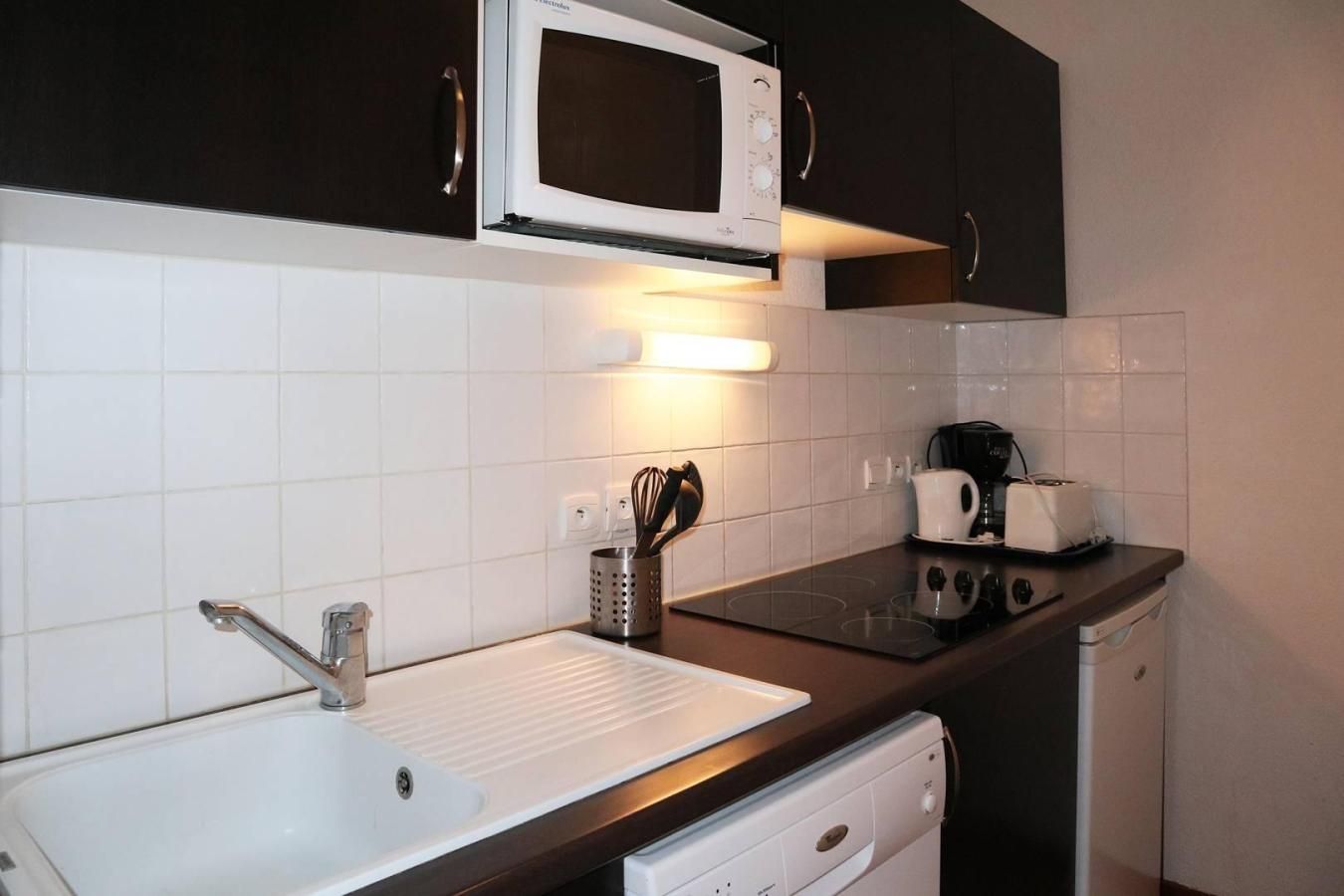 Een kleine keuken met een witte spoelbak, een magnetron, een broodrooster en een koffiezetapparaat.