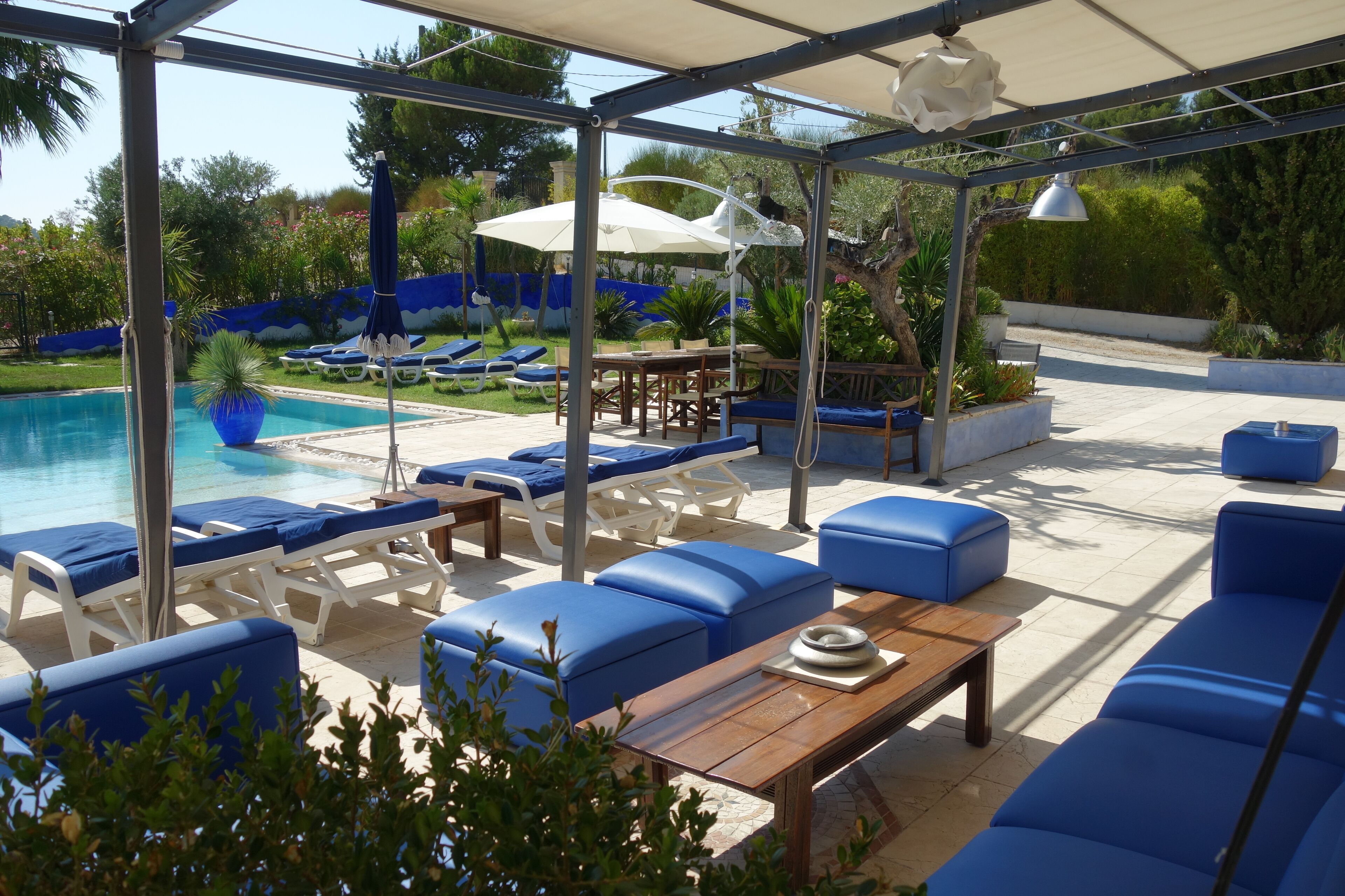 Un espace extérieur aménagé, abrité, avec des fauteuils de jardin bleus et une piscine.