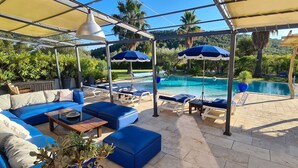 A covered outdoor area with a pool, blue lounge chairs, and a sofa. - Superb luxury villa rental with heated pool (Le Castellet)