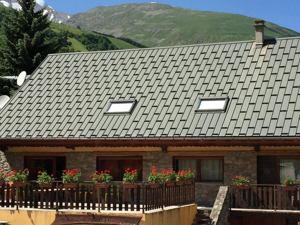 A chalet-style building with a sloped roof, stone walls, and a wooden fence with flower boxes. - 350m from shops, 1st floor, fitness, sauna, hammam, balcony, fireplace or stove, ski locker, 55m² (Valloire)