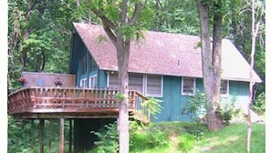 A house with a wooden deck and a large tree in front.