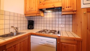A compact kitchen with wooden cabinets, a gas stove, a coffee maker, and a dishwasher.