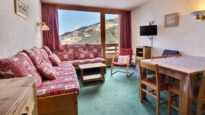 A cozy room with a sofa, a dining table, a TV, and a view of a mountainous landscape.