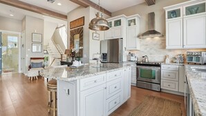 Una cocina amplia con armarios blancos, una isla grande, electrodomésticos de acero inoxidable y una lámpara colgante.