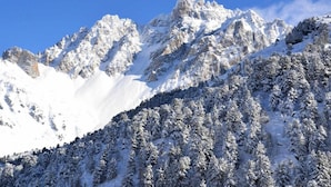 A snow-covered mountain landscape with rocky peaks and dense forests.