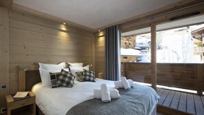 Un dormitorio moderno con una cama grande, paredes de madera, un balcón con vistas y una mesita de noche con una lámpara.