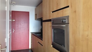 A kitchen with wooden cabinets, a red door, and a stainless steel oven. - 50m from ski lifts, 4th floor, view mountain, balcony, tv, 30m², Les Arcs (Les Arcs)