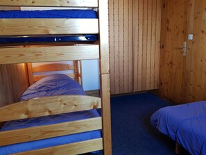 A bunk bed with a blue mattress, a wooden headboard, and a wooden wall paneling.