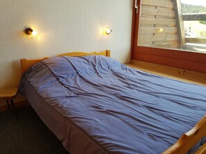 A small room with a single bed, a wooden chair, and two wall-mounted lights.