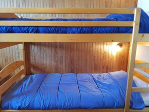 Uma cama beliche com roupa de cama azul num quarto com paredes de madeira.