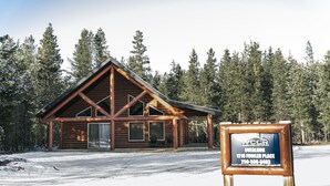 A log cabin with a pitched roof, a porch with chairs, and a signboard in front. - Overlook Cabin Rental - Pet Friendly! (Valemount)