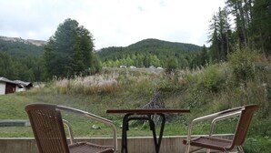 An outdoor seating area with two wicker chairs and a small table, overlooking a mountainous landscape with a cabin in the background. - Ski-in/ski-out & foot of the slopes, 1st floor, view swimming pool, swimming pool, sauna, hammam (Les Orres)