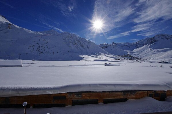 A snow-covered landscape with a wooden building in the foreground and mountains in the background.