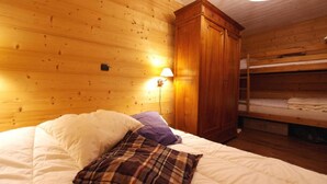 Une chambre de cabane en bois avec un lit superposé, un lit simple avec un oreiller à carreaux, une armoire en bois et une lampe fixée au mur.
