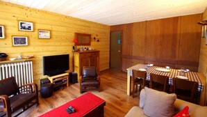 L’intérieur chaleureux d’un chalet, avec un décor en bois, une table à manger pour quatre personnes, un téléviseur et une cheminée.
