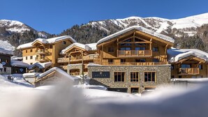 Un chalet en bois doté de plusieurs balcons et d’une façade en pierre, entouré de montagnes enneigées.